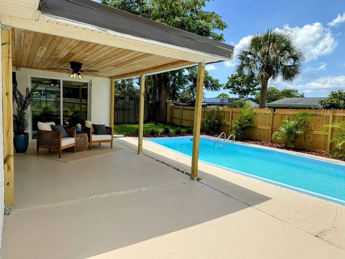 Finished rectangular pool beside a new covered patio, palms and a cedar fence