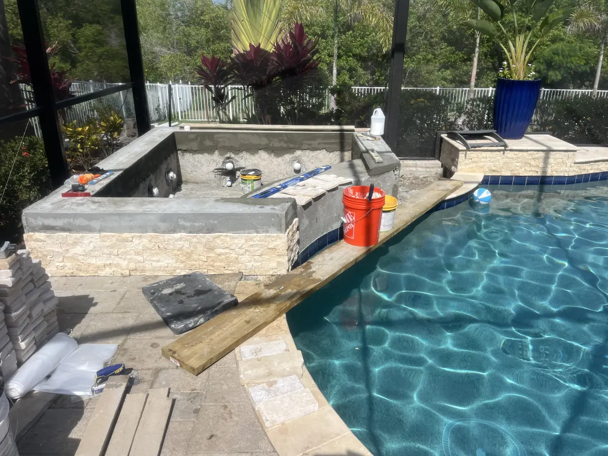 A raised spa mid-construction, with stacked stone veneer and a pool beyond